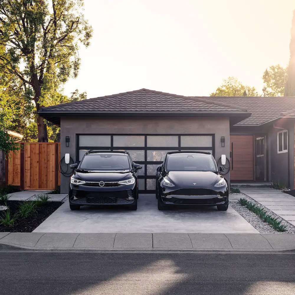 Electric cars charging in residential garage driveway.