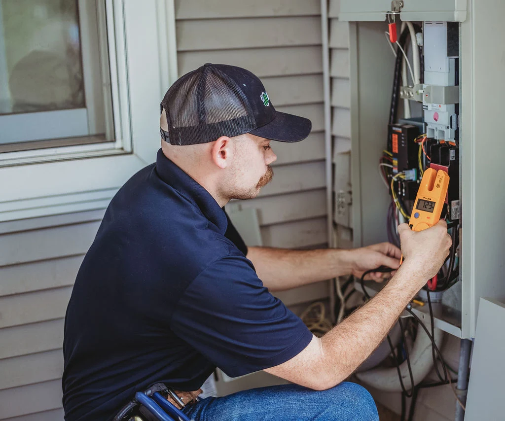 Electrician checking outdoor electrical panel with multimeter.