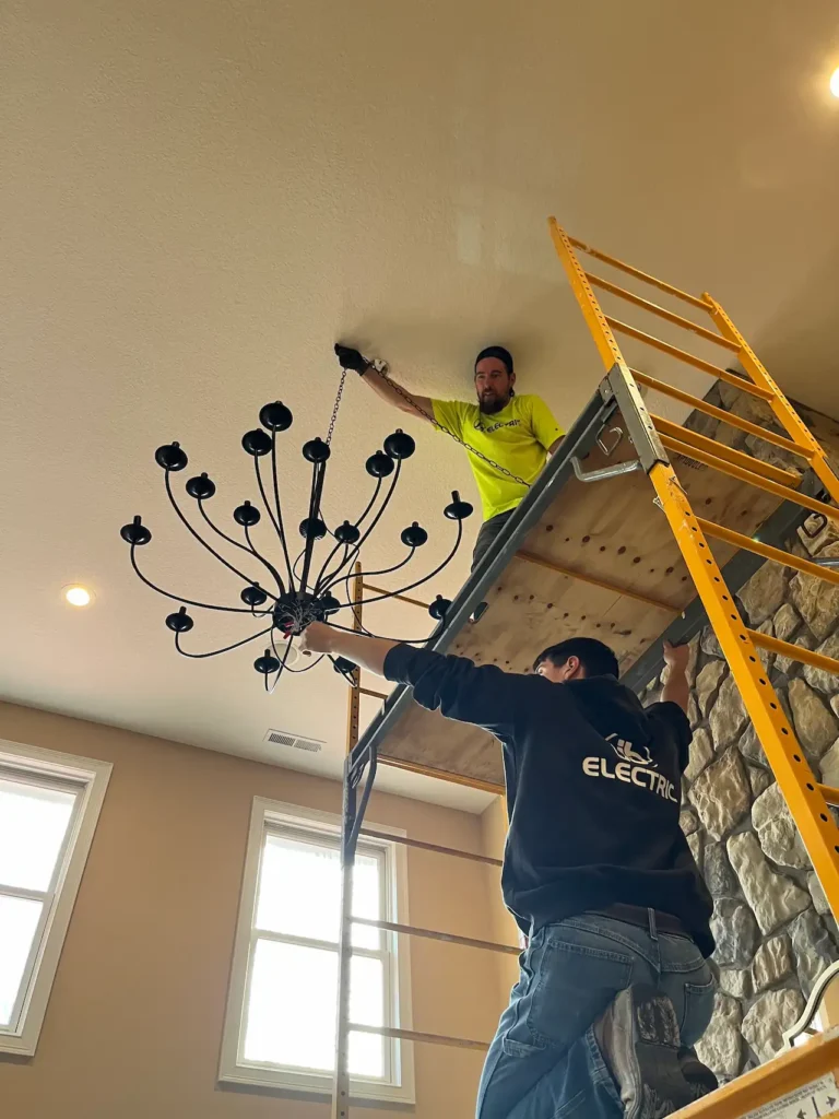 Two workers installing ceiling chandelier with scaffolding.