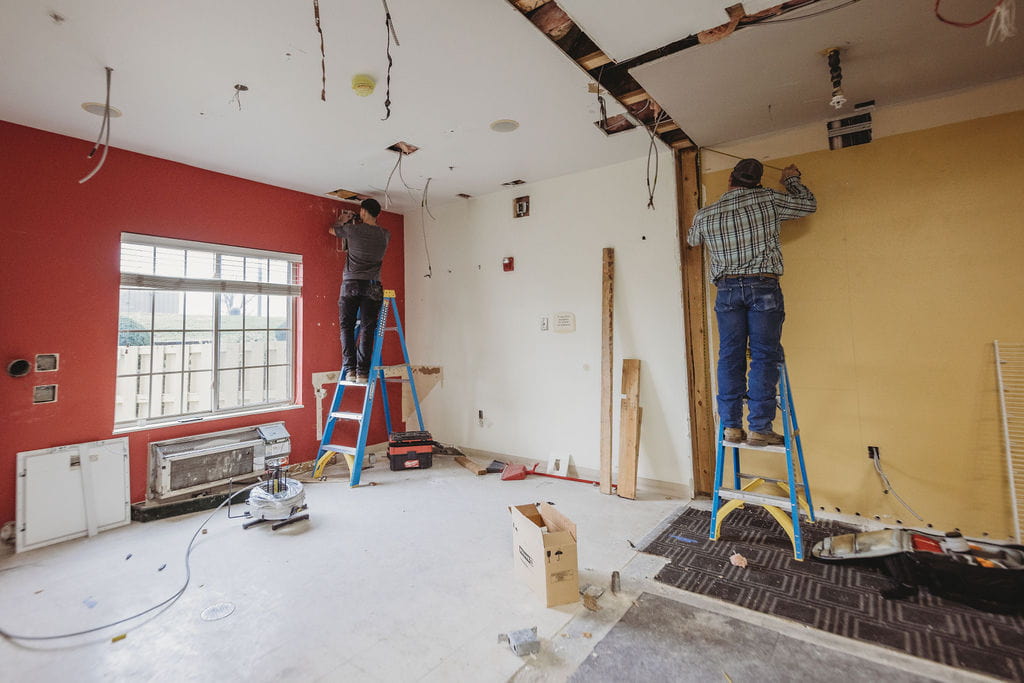 Workers renovating a room with ladders and tools.