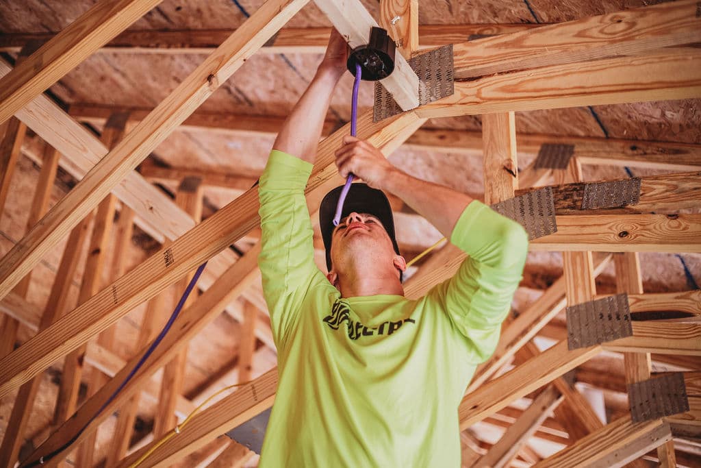 Electrician installing wiring in wooden ceiling framework.