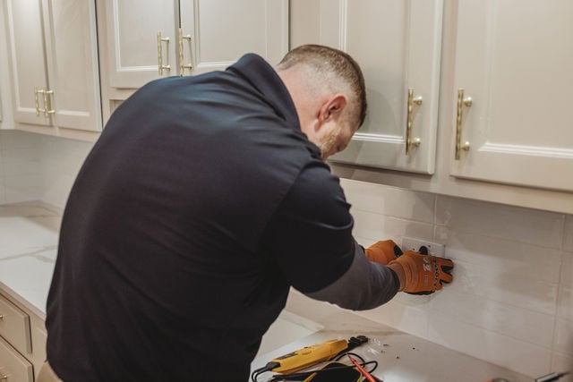 Electrician installing kitchen outlet with tools.