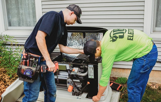 Workers repairing a home generator outside.